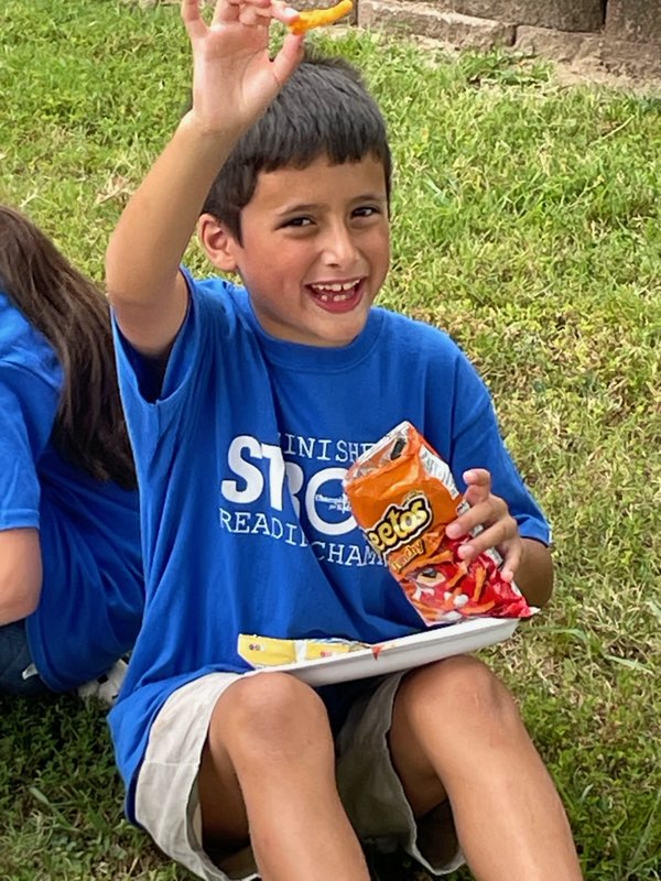 A boy holding onto some chips while sitting on the grass.