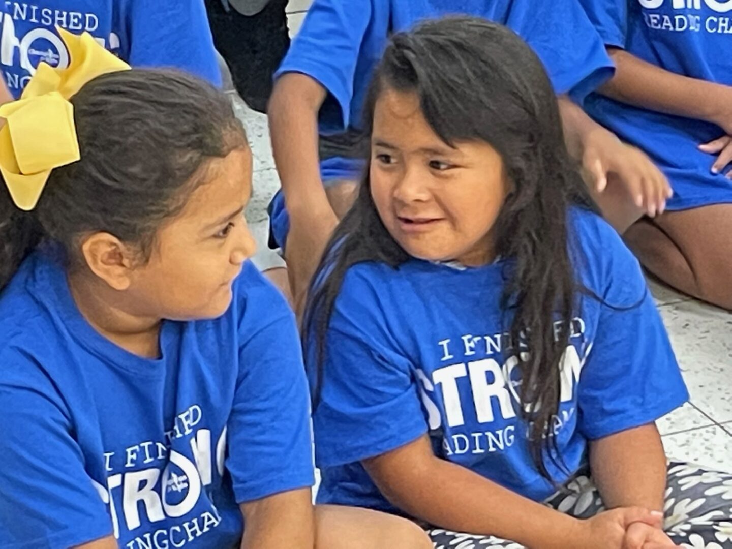 Two girls in blue shirts are sitting next to each other.