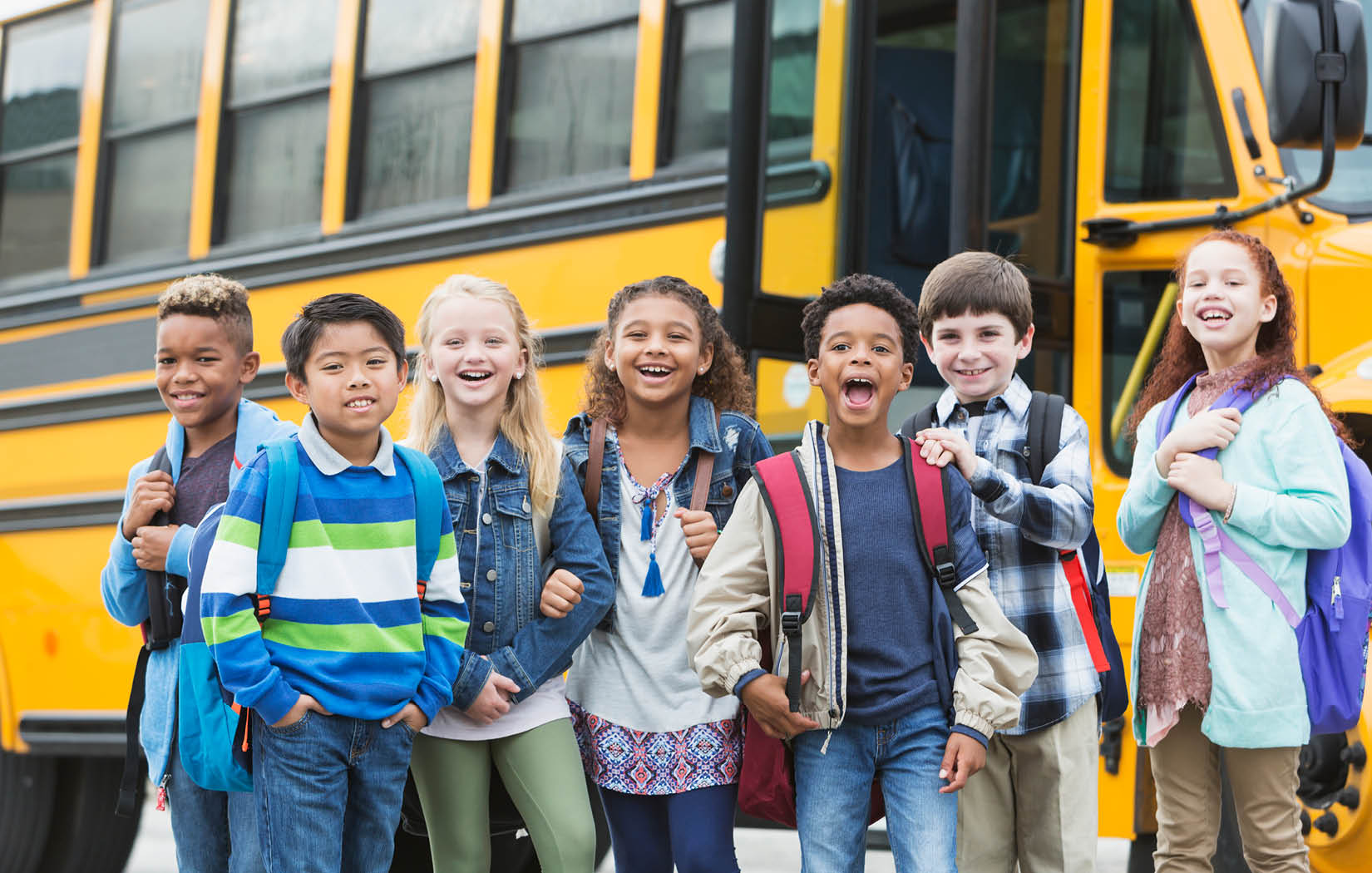 A group of kids standing in front of a school bus.