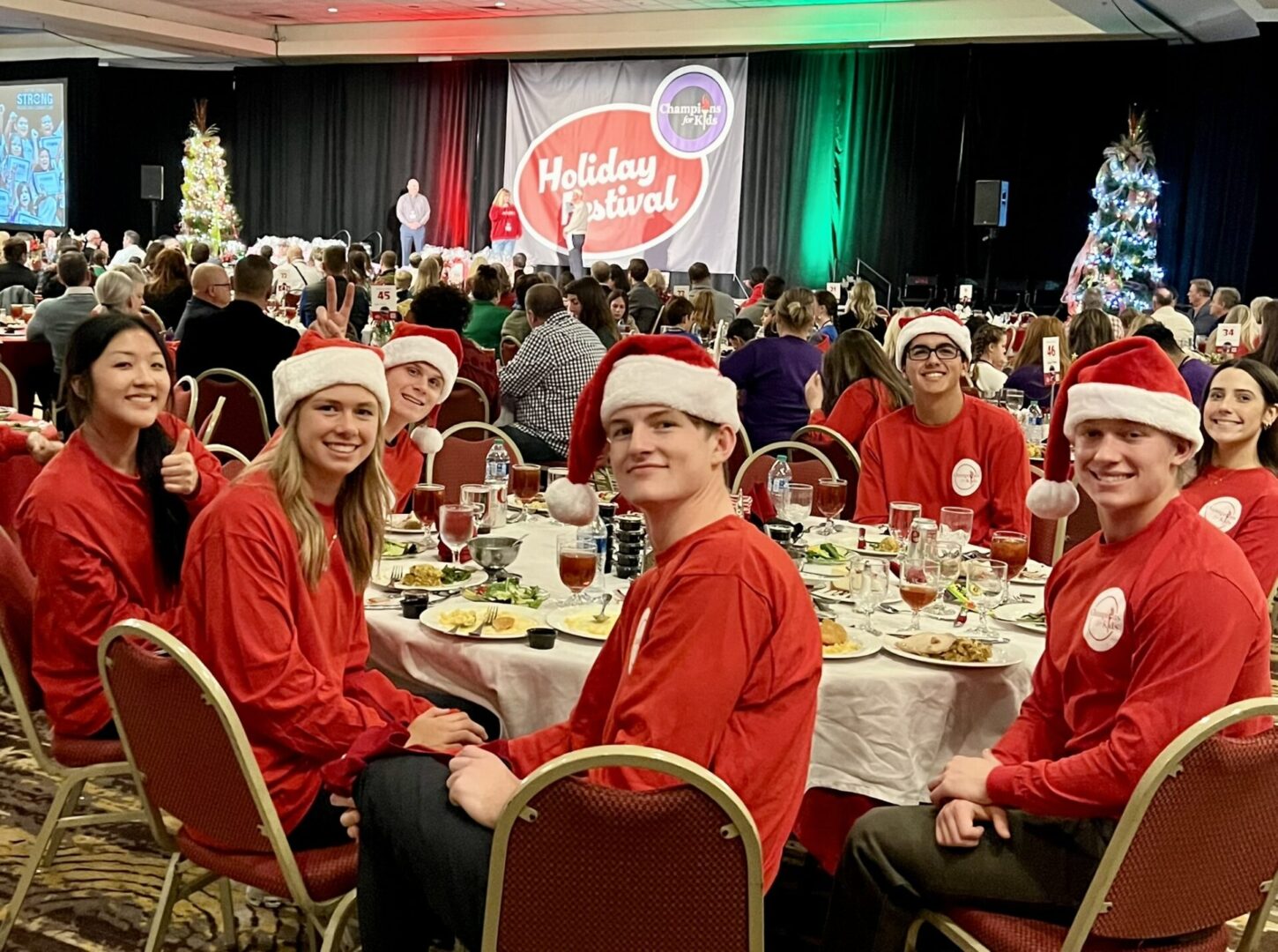 A group of people sitting at tables with christmas decorations in the background.